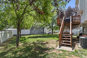Fenced backyard with a trampoline, a wooden deck, and stairs