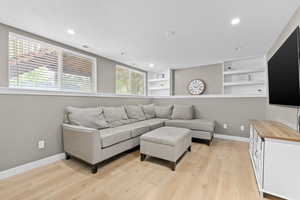 Living area with a textured ceiling, light wood-style flooring, built in features, and recessed lighting
