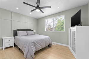 Bedroom featuring light wood finished floors, recessed lighting, a ceiling fan, a textured ceiling, and a decorative wall