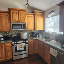 Kitchen featuring stainless steel appliances, tasteful backsplash, dark wood-style flooring, vaulted ceiling, and light countertops