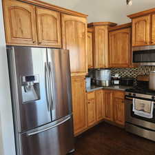 Kitchen with stainless steel appliances, tasteful backsplash, dark wood-style floors, and brown cabinets
