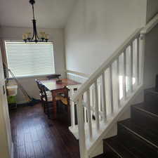 Dining room featuring dark wood-style flooring, vaulted ceiling, a chandelier, and stairs