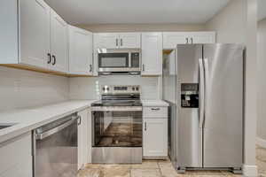 Kitchen featuring stainless steel appliances, decorative backsplash, light countertops, and white cabinets