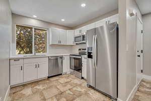 Kitchen with stainless steel appliances, decorative backsplash, recessed lighting, white cabinets, and light countertops