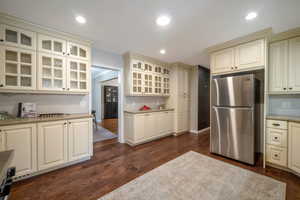 Kitchen featuring freestanding refrigerator, dark wood finished floors, cream cabinets, light stone countertops, and recessed lighting