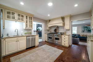 Kitchen with stainless steel appliances, dark wood-style floors, premium range hood, glass insert cabinets, and light stone counters