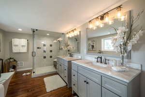Bathroom featuring two vanities, a shower stall, and wood finished floors