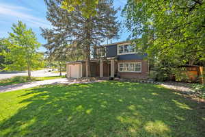 View of front of property featuring brick siding, concrete driveway, a front lawn, and a garage