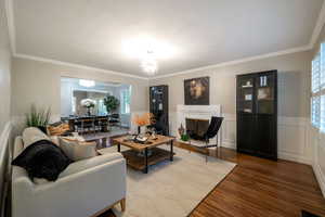 Living area with wood finished floors, a chandelier, crown molding, and wainscoting