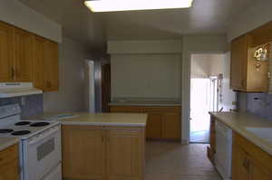 Kitchen with decorative backsplash, white appliances, exhaust hood, and light countertops