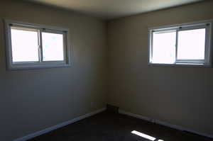 Unfurnished room featuring healthy amount of natural light and dark carpet