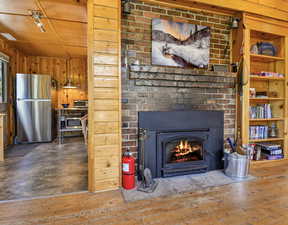Detailed view of freestanding refrigerator, wood walls, wood finished floors, and a brick fireplace