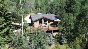 Back of property featuring a standing seam roof, a wooded view, a metal roof, and a deck
