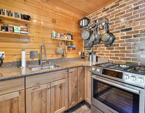 Kitchen featuring stainless steel gas range oven, stone counters, and wooden walls
