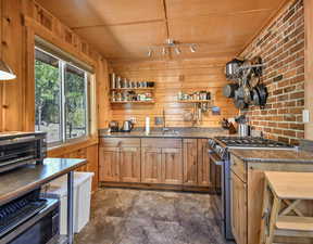 Kitchen featuring wood walls, appliances with stainless steel finishes, open shelves, dark stone counters, and dark stone finish flooring