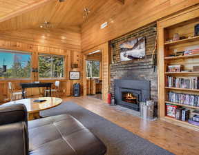 Living room featuring hardwood / wood-style flooring, a fireplace, wood walls, wood ceiling, and high vaulted ceiling