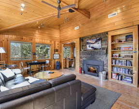 Living area featuring wood finished floors, a brick fireplace, wooden walls, a wood ceiling with exposed beams, and ceiling fan