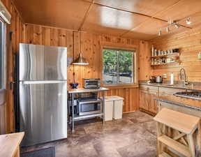 Kitchen with appliances with stainless steel finishes, open shelves, stone counters, and wooden walls