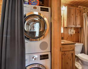 Laundry area featuring stacked washer and clothes dryer and wood walls