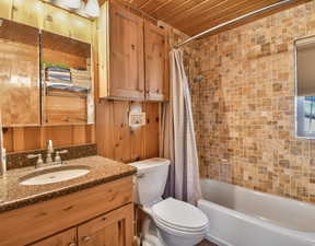 Bathroom with wooden ceiling, vanity, shower / bath combo with shower curtain, and wooden walls