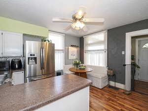 Kitchen with stainless steel refrigerator with ice dispenser, dark wood-style flooring, a textured ceiling, a peninsula, and dark countertops