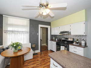 Kitchen with gas stove, dark wood-style flooring, a textured ceiling, dark countertops, and white cabinetry