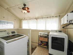 Washroom featuring separate washer and dryer, light tile patterned floors, wooden walls, ceiling fan, and cabinet space