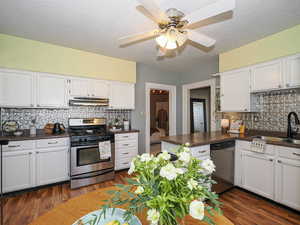 Kitchen with decorative backsplash, stainless steel appliances, dark countertops, white cabinets, and a textured ceiling