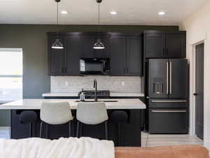 Kitchen featuring high end fridge, light countertops, a kitchen island with sink, black microwave, and a breakfast bar area