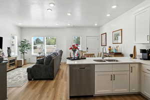 Kitchen with open floor plan, a peninsula, stainless steel dishwasher, light wood-style floors, and a textured ceiling