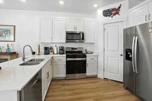 Kitchen featuring appliances with stainless steel finishes, a peninsula, light wood finished floors, recessed lighting, and white cabinets