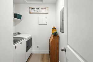 Laundry room with washing machine and clothes dryer, light wood-type flooring, and electric panel