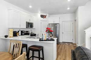 Kitchen with a peninsula, appliances with stainless steel finishes, a breakfast bar, light wood-style flooring, and light countertops