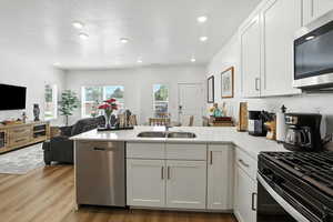 Kitchen with a peninsula, appliances with stainless steel finishes, light countertops, light wood-style floors, and white cabinetry