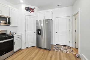 Kitchen featuring stainless steel appliances, white cabinetry, light wood-type flooring, and light countertops