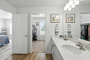 Ensuite bathroom with wood finished floors, double vanity, a spacious closet, and a textured ceiling