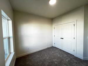 Unfurnished bedroom featuring dark colored carpet and a closet