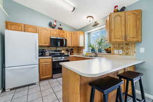 Kitchen with stainless steel appliances, lofted ceiling, a peninsula, light countertops, and light tile patterned flooring