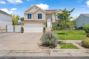 Bi-level home with brick siding, concrete driveway, a garage, stucco siding, and a gate