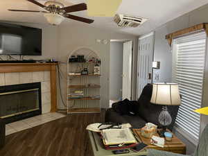 Living area featuring cooling unit, wood finished floors, a tile fireplace, and ceiling fan