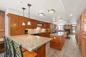 Kitchen featuring brown cabinetry, a textured ceiling, a peninsula, light stone countertops, and a stone fireplace