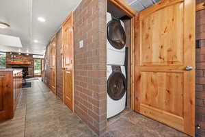 Laundry room featuring stacked washer / dryer, brick wall, a textured ceiling, a fireplace, and wooden walls