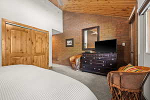 Bedroom with brick wall, vaulted ceiling, carpet floors, and wooden ceiling