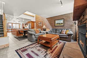 Living area featuring brick wall, a glass covered fireplace, a textured ceiling, light tile patterned flooring, and stairs