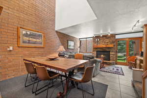 Dining room with a textured ceiling, a stone fireplace, light tile patterned floors, brick wall, and rail lighting