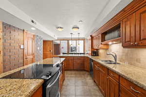 Kitchen featuring range with electric cooktop, light stone counters, a textured ceiling, brown cabinets, and a peninsula