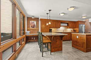 Kitchen with brown cabinets, a center island, a kitchen breakfast bar, pendant lighting, and tasteful backsplash
