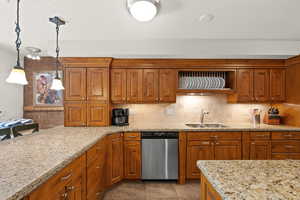 Kitchen featuring stainless steel dishwasher, decorative backsplash, brown cabinets, light stone counters, and a textured ceiling