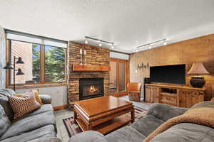 Living room featuring a fireplace, tile patterned flooring, a textured ceiling, track lighting, and brick wall
