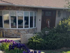 Doorway to property featuring brick siding and roof with shingles